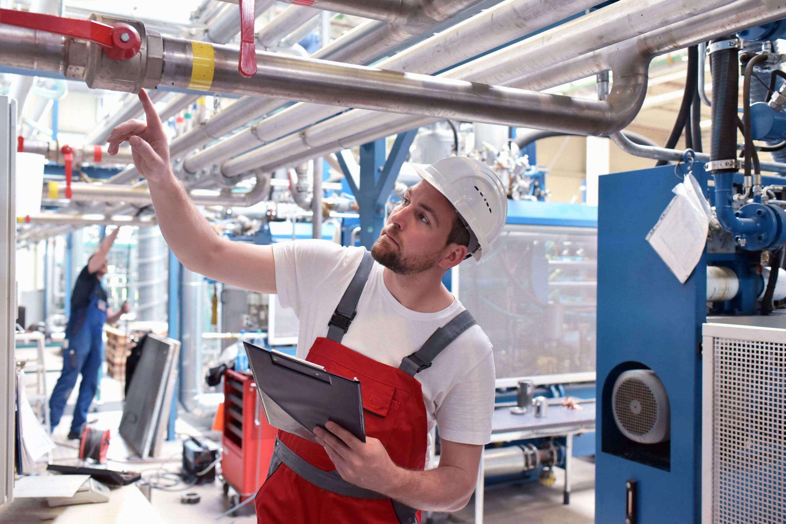 Ein Mitarbeitender, welcher in einer modernen Produktionshalle Anlagen und elektrische Komponenten prüft